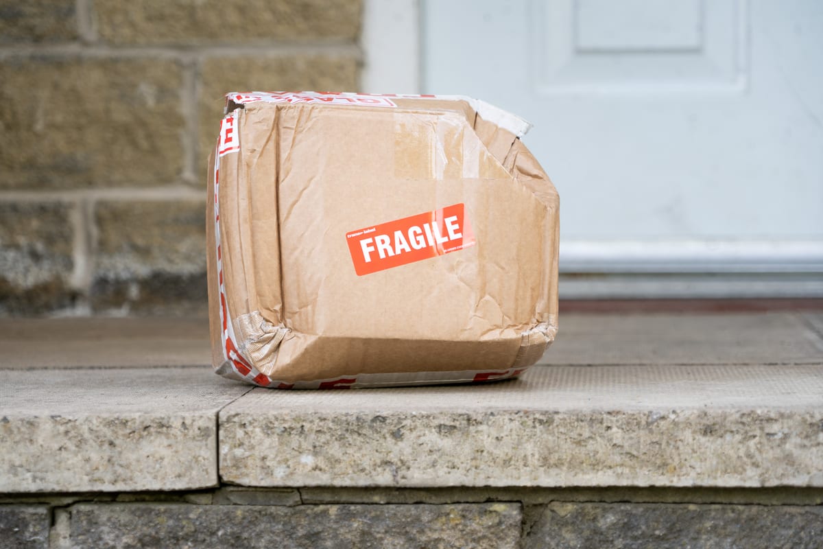 Sammenklemt pakke merket «Fragile» satt igjen på en dørterskel